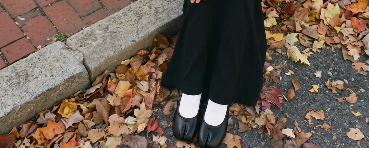 Ballerines tabi noires et chaussettes blanches sur un trottoir couvert de feuilles d'automne